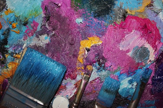 Picture of a color palette and a few paint brushes. The overall tint is pink, purple and blue. 