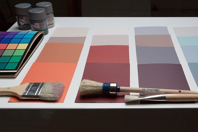 Picture of a palette of colors lying a table. On the color palettes there are 3 paint brushes and some paint in the corner. 