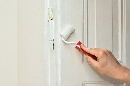 Picture of a hand holding a roller and painting the door in white. 