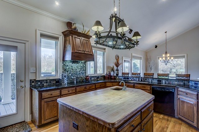 Picture of a kitchen. In the center of the photo you see a kitchen island with a wooden countertop. Around the island you see the rest of the kitchen, with a lot of dark brown cabinets.